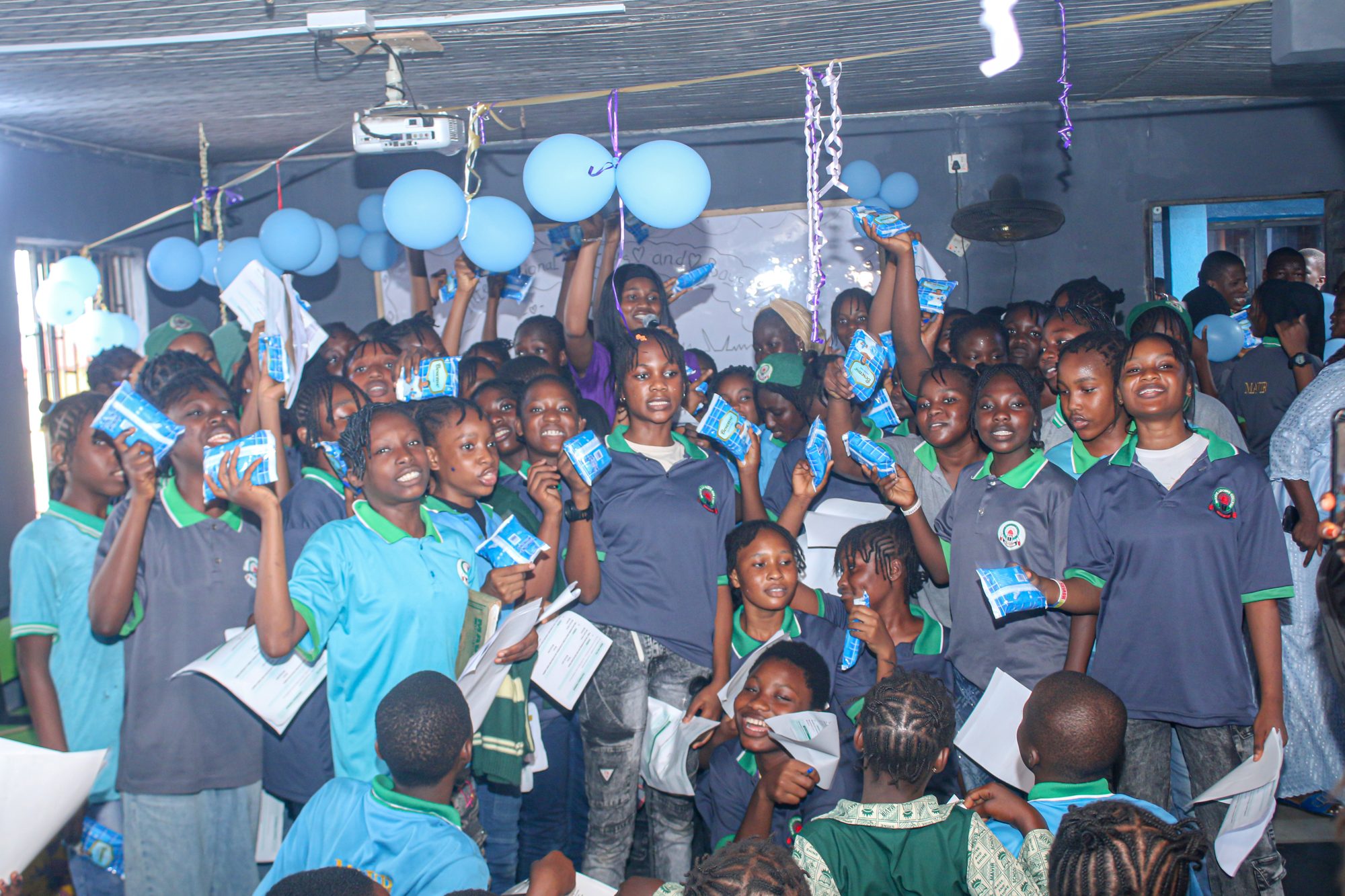 Girls at Mavir Leaders College holding up sanitary pads and handouts at the GLYE International Day of the Girl celebration, October 2026